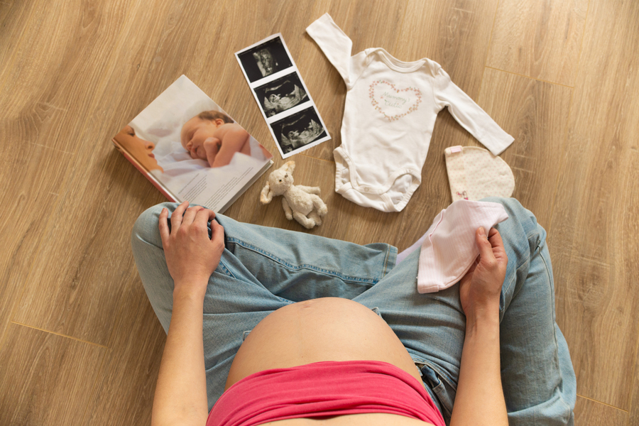 pregnant-woman-with-white-baby-bodysuit-socks-hat-ultrasound-image-preparing-childbirth-pregnancy-young-mother-sitting-floor.jpg